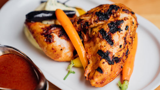 A roast half chicken with heirloom carrots being drizzled with citrus sauce.