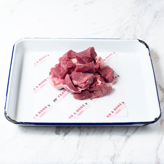 Diced lamb on a white and navy enamel tray on a marble bench.