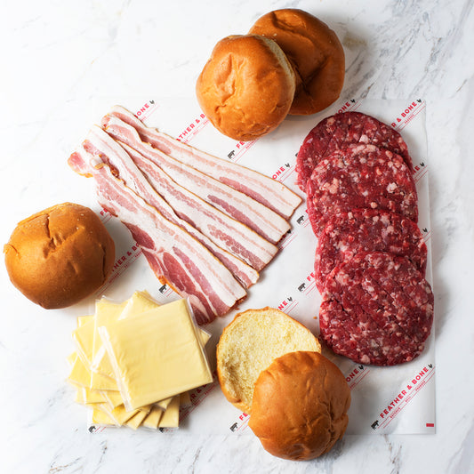 Four burger patties, cheese, bacon & burger buns on Feather & Bone branded paper.