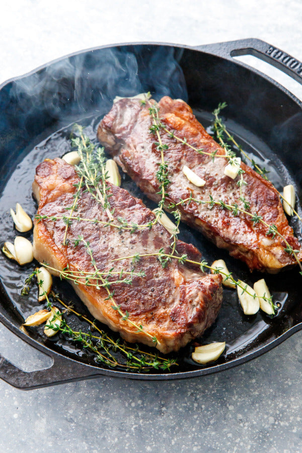 Steak searing in a pan with thyme and garlic.