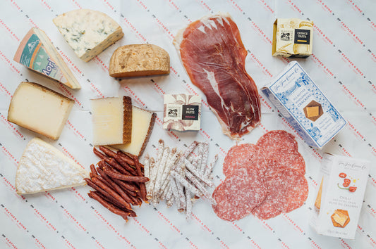 Cheeses, preserved meats, pastes and crackers laid out on Feather & Bone branded butcher's paper.
