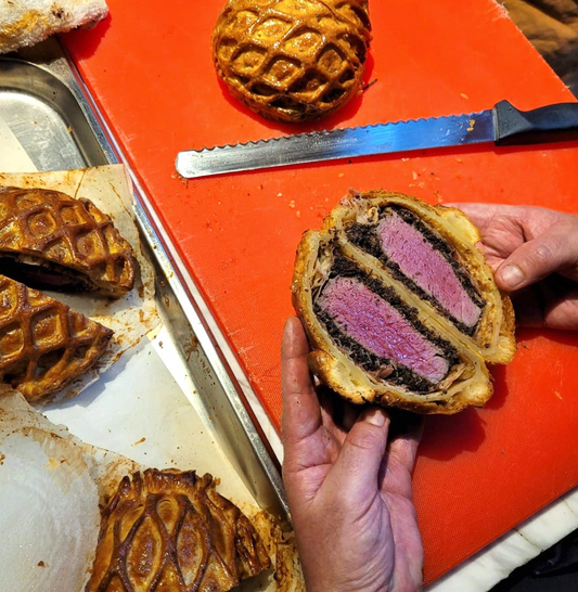 A golden beef wellington cut open to show the blushing beef tenderloin within.
