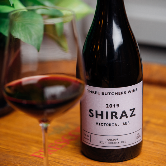 A bottle of Three Butchers Shiraz behind a glass of the same wine.