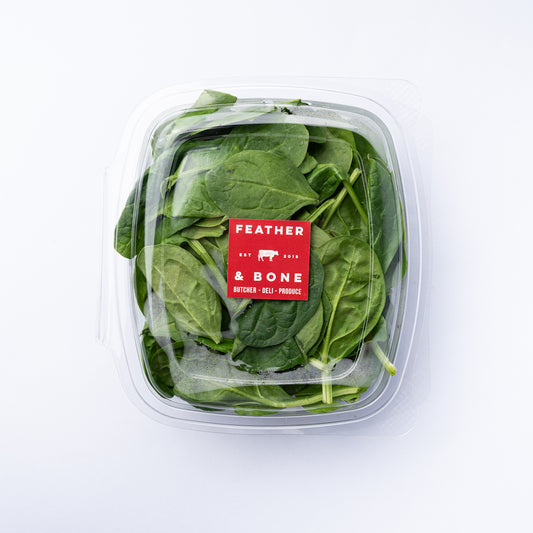 A plastic box of spinach leaves with a square red Feather & Bone label.