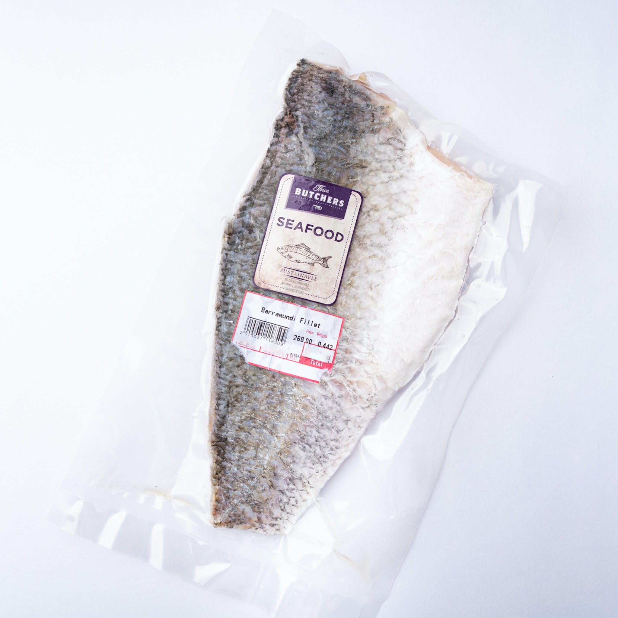 A frozen Barramundi Fillet with the silvery skin on in a vacuum bag with a purple label saying Three Butchers Fish.