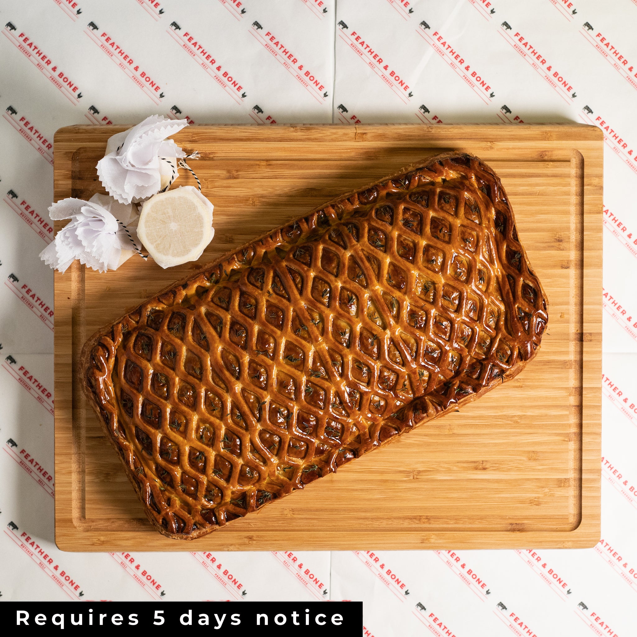 An ornate SALMON EN CROÛTE 1.5kg wrapped in decorative pastry on a board with lemon halves wrapped in muslin.