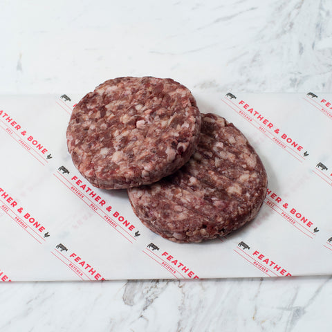 Two dry aged beef patties on Feather & Bone branded paper.