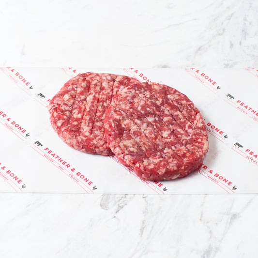 Two Grass Fed Beef Patties on a marble slab.