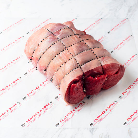 A boned, rolled and tied leg of lamb on a marble slab.