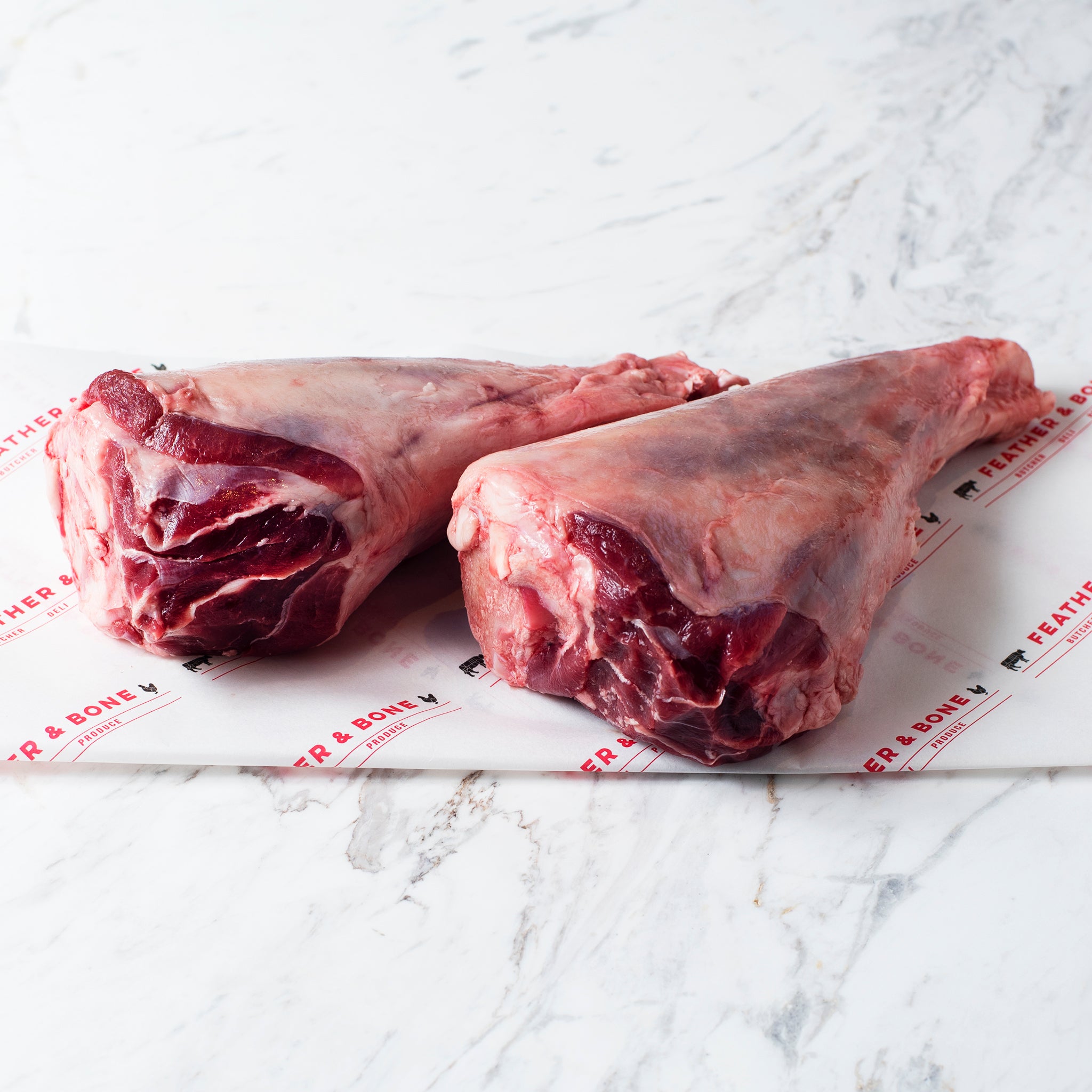 Two lamb shanks on a marble slab.