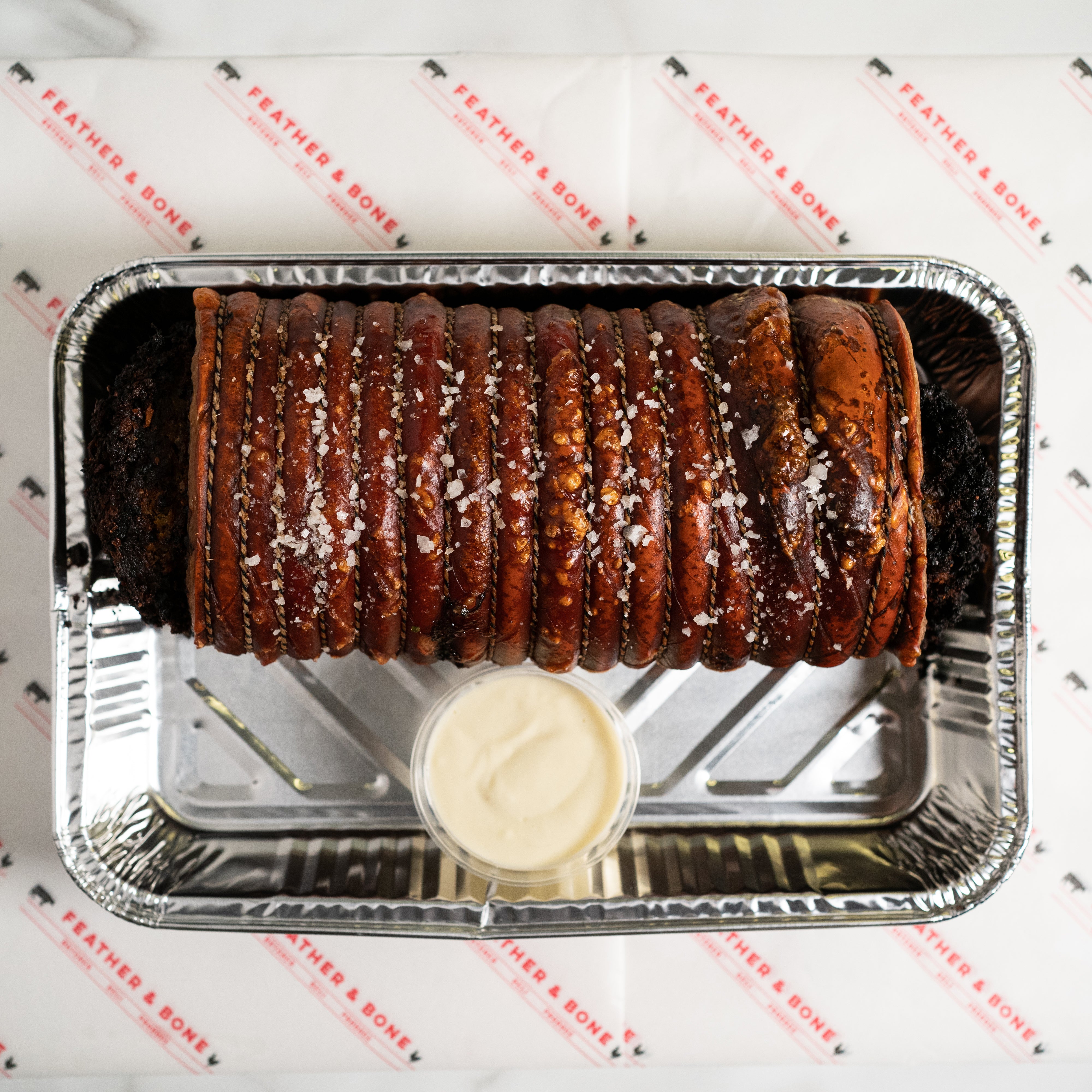 A beautiful rolled, tied and roasted porchetta in a foil tray.