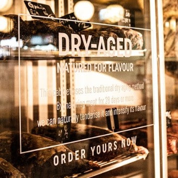 The glass door of a dry-ager with Dry-Aged written in gold lettering on it.