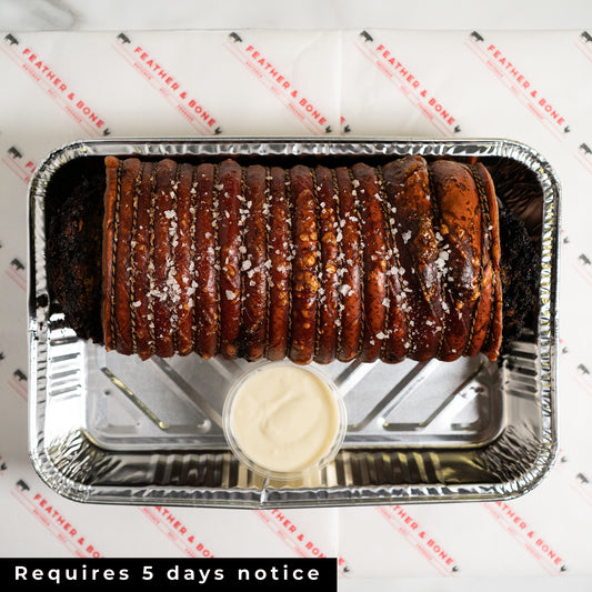 A golden roasted porchetta with apple sauce in a foil tray.