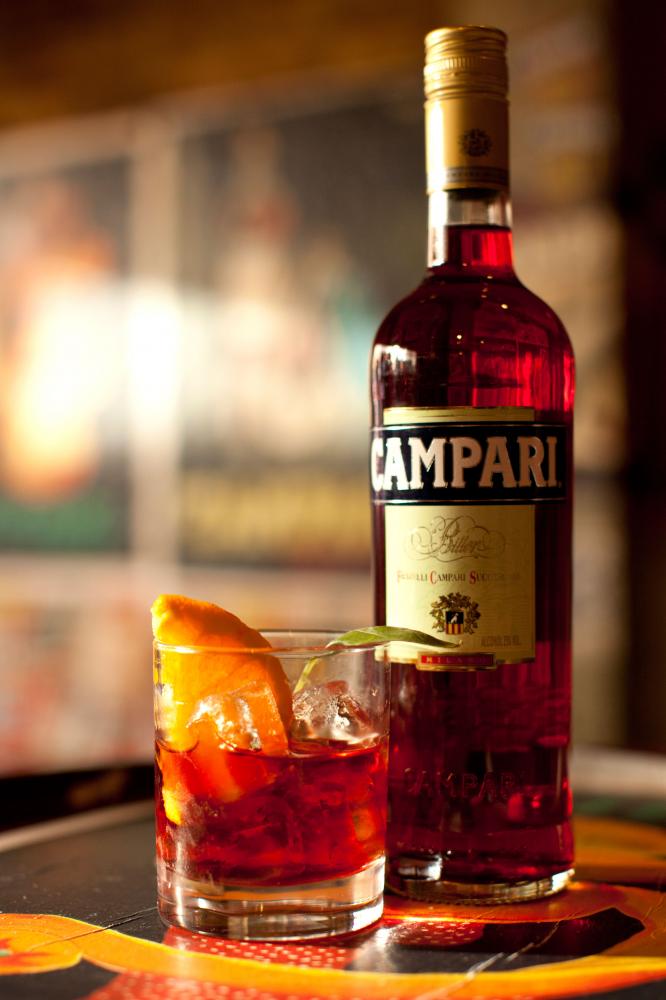 Campari with ice and an orange wedge in a glass in front of a bottle of Campari.